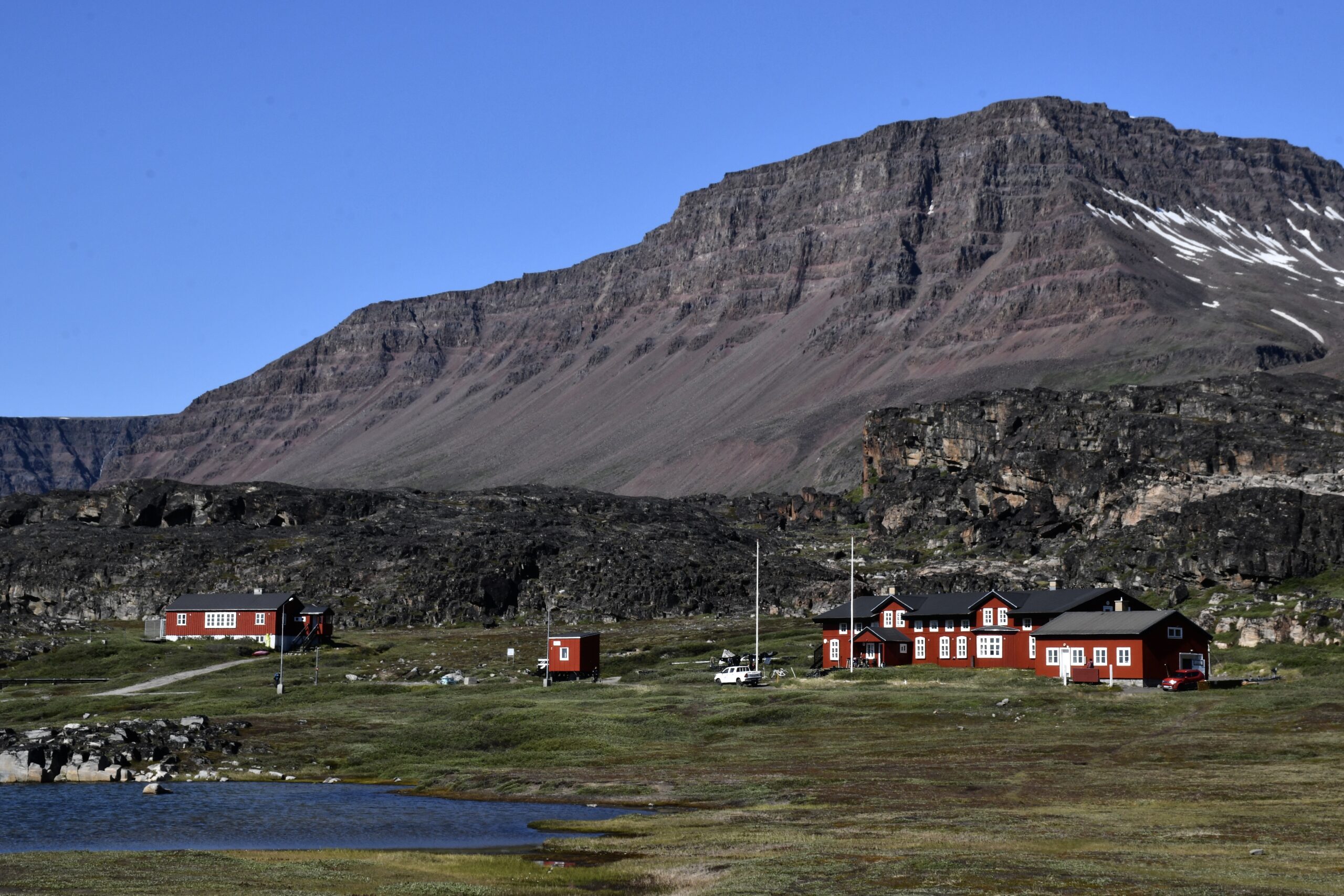 Store dele af Discoøen består af stejle, rødbrune og lagdelte basaltfjelde, der opstod gennem vulkansk aktivitet for 50-80 mio. år siden. De højeste fjeldtoppe rækker over 2.000 meter op. De røde bygninger rummer Arktisk Station, der forsker i klimaforandringer. Foto: Niels Lyksted